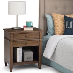 a night stand with a lamp on top of it next to a bed and pillows