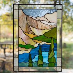 a stained glass window hanging from the side of a building with mountains in the background