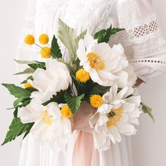 a woman holding a bouquet of white and yellow flowers in her hands with lace on the sleeves