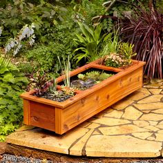 a wooden planter filled with plants on top of a stone walkway next to trees