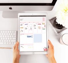 a person is using an ipad on a desk with a keyboard, mouse and flowers