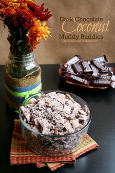 a glass bowl filled with muddy buddies next to a vase full of flowers and chocolate bars