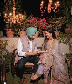 a man and woman sitting next to each other in front of some potted plants