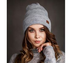 a woman with long hair wearing a gray sweater and a knitted beanie hat