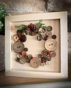 a white frame with buttons and pine cones in it on a table next to a potted plant