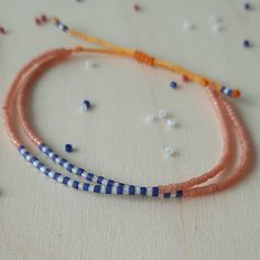 two bracelets with blue and orange beads on a white tablecloth, one has an orange string