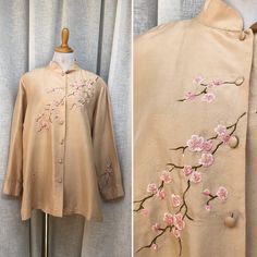 "Beautiful beige/rose gold silk mandarin high neck blouse with pink cherry blossom embroidery by Yi Lin. Button down with fabric wrapped buttons, lightly padded shoulders, and two side slits. Good vintage condition, two small water stains on the back of the blouse (see pictures)  Marked size 1X Measures (flat) Shoulder to shoulder: 17.5\" armpit to armpit: 24\" Sleeve length: 22\" Shoulder to hem length: 28\"" Spring Blouse With Stand Collar And Buttons, Spring Top With Stand Collar And Button Closure, Spring Top With Button Closure And Stand Collar, Spring Top With Stand Collar, Embroidered Spring Blouse With Stand Collar, Spring Embroidered Blouse With Stand Collar, Embroidered Stand Collar Blouse For Spring, Embroidered Blouse With Stand Collar For Spring, Traditional Spring Tops With Stand Collar