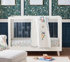 a baby crib in the corner of a room with blue walls and floral wallpaper