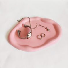 a pink tray with jewelry on top of it and a pair of earbuds in the middle