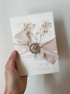 a hand holding a wedding card with flowers on the front, and a ribbon tied around it