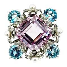 An absolutely gorgeous brooch that everyone will notice! Designed and created by Bielka, this brooch features a 60.00 carat step cut Kunzite, framed in a Diamond, Pearl and Blue Topaz floral motif made all in platinum. The Diamonds are round brilliant cut, and have a total weight of 2.64 carat, set with four cultured Pearls, and four Blue Topaz that have a total weight of 28.03 carats. The back of the brooch features a double pin, and is signed "BIELKA", and stamped "PLAT". Offered by Charles Sc Luxury Multi-stone Brooches For Anniversary, Elegant Multi-stone Collectible Brooches, Formal Multi-stone Brooch In Fine Jewelry Style, Formal Multi-stone Brooch Fine Jewelry, Formal Multi-stone Brooches In Fine Jewelry Style, Elegant Multi-stone Brooches For Formal Occasions, Fine Jewelry Multi-stone Wedding Brooches, Luxury Evening Gemstone Brooches, Unique Gemstone Brooch For Formal Wear