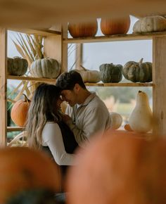 a man and woman standing next to each other in front of shelves filled with pumpkins