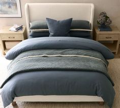 a bed with blue comforters and pillows in a small room next to two nightstands