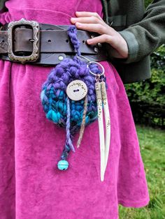 a woman wearing a pink dress holding a purple and blue crochet belt with scissors attached to it