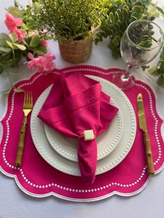 the place setting is set with pink napkins, silverware and green plants in vases