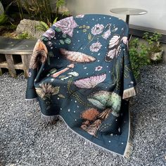 a chair covered in a blue blanket with flowers and butterflies on it sitting next to a table