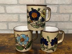 three coffee mugs sitting next to each other on top of a wooden table in front of a brick wall