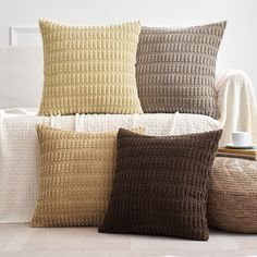 four pillows on a couch in front of a white chair with a coffee cup sitting on it