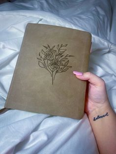 a woman's hand holding a brown book with flowers on it