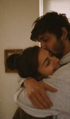 a man and woman embracing each other in front of a window with their eyes closed