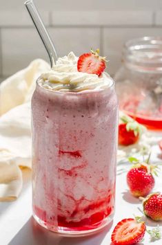 a strawberry milkshake with whipped cream and fresh strawberries on the table next to it