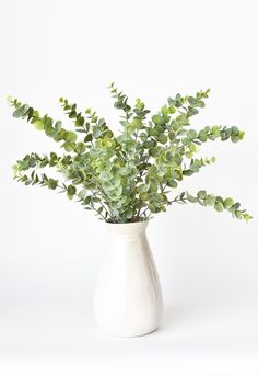 a white vase filled with green leaves on top of a table