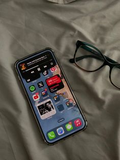 an iphone is laying on a bed next to some reading glasses and a pair of eyeglasses