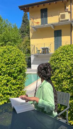 a woman sitting at an outdoor table reading a book in front of a yellow building