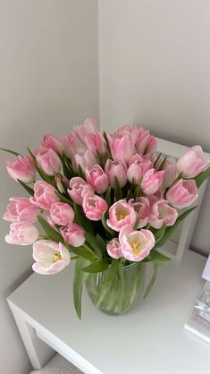 a glass vase filled with pink tulips sitting on top of a white table