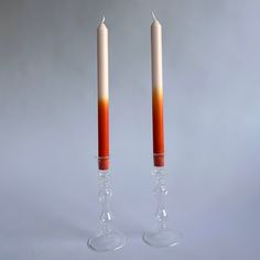 two candles with orange and white wax on them are standing next to each other in wine glasses