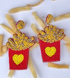 two red and yellow beaded earrings with hearts on them sitting next to french fries