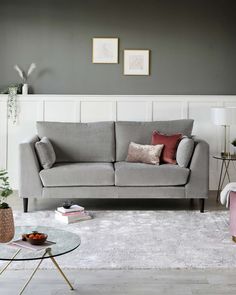 a living room with grey walls and white carpeted flooring, two couches in front of a glass coffee table