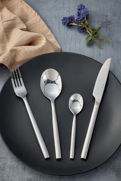 four forks, two spoons and one knife on a black plate next to blue flowers