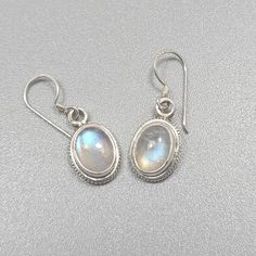 Sterling silver earrings with blue moonstone settings. Classical style, gemstones have a pretty blue reflection. Dimensions with hook: 25mm x 9mm, or 0.98 inch x 0.35 inch. Dimensions pattern: 11mm x 9mm, or 0.43 inch x 0.35 inch.  Gemstone 8mm x 6mm, or 0.31 inch x 0.24 inch. Weight silver and gemstone: 2.8gm/0.10oz Silver Nickel-free Moonstone Earrings, Hypoallergenic Silver Moonstone Jewelry, Round Moonstone Cabochon Earrings, Silver Moonstone Gemstone Earrings, Silver Moonstone Earrings With Ear Wire, Silver Cabochon Dangle Earrings, Sterling Silver Oval Cabochon Earrings, White Oval Moonstone Earrings, Silver Oval Cabochon Earrings