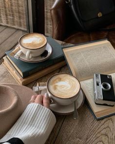 a person sitting at a table with books, camera and cappuccino in front of them