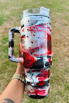 a hand holding a large glass with red and black paint on it in the grass