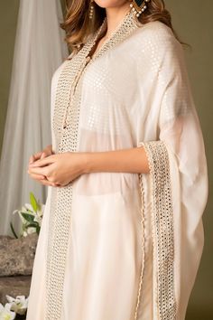 Ivory cape with mirror embroidered borders. Comes with embroidered blouse and sharara.
Component: 3
Pattern: Embroidery
Type Of Work: Mirror work
Neckline: Cape: Open
Sleeve Type: Blouse: Half, Cape: Three quarter
Fabric: Organza, Silk
Color: Ivory
Other Details: 
Attached lining
Approx weight (in kgs): 3
Closure: Sharara: Button
Occasion: Destination Wedding - Aza Fashions Elegant Beige Sharara With Sheer Dupatta, Traditional Wedding Kaftan With Sheer Dupatta, Elegant Long Beige Kurta, Transitional White Kaftan, Cream Blouse Piece With Cutdana For Eid, White Anarkali Blouse With Sheer Dupatta, Elegant Cream Sharara With Sheer Dupatta, Anarkali Gota Work Kaftan For Wedding, White Kaftan With Dupatta For Wedding