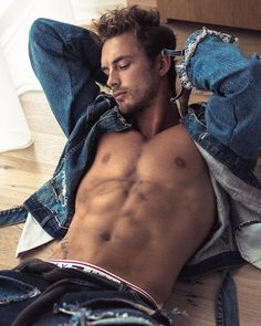 a shirtless man laying on the floor with his hands in his hair and jeans