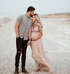 a man and woman standing next to each other on a dirt road in front of the ocean