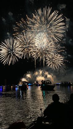 fireworks are lit up in the sky above water and boats on the water at night