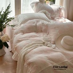 there is a bed with white sheets and pillows on it, next to a vase with flowers