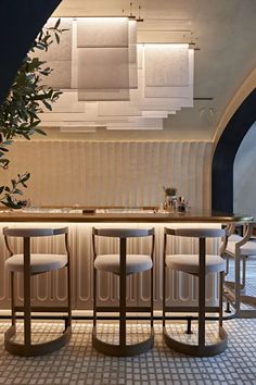 a bar with four stools and a plant in the corner next to it on a tiled floor