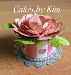 there is a pink flower that is in a cupcake box with green leaves on it