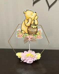 a winnie the pooh birthday cake topper on a wooden table with flowers and an ornament