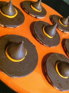 an orange tray filled with chocolate donuts covered in brown icing and topped with small gray hats