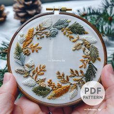 someone is holding up a hand embroidered christmas ornament with pine cones and leaves