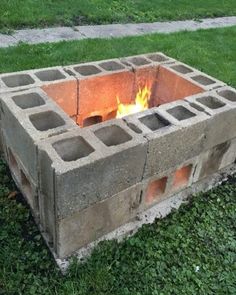 a fire pit made out of cinder blocks in the grass with flames coming from it