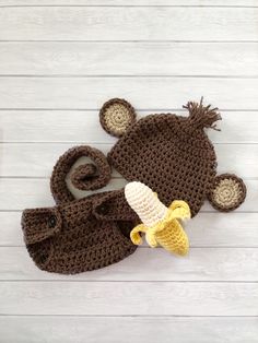 a crocheted hat and booties are on a white wooden table with a banana