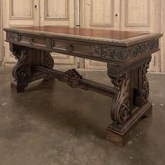 an antique desk with intricate carvings on the top and bottom, in front of a wooden paneled wall