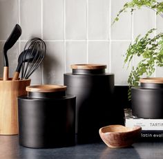 black kitchen utensils and wooden spoons are on the counter next to books